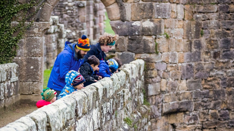 A family peer over a wall at Fountains Abbey and Studley Royal Water Garden, North Yorkshire
